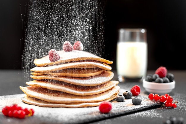 Large american pancakes on a dark background breakfast european chef sprinkles pancakes with powdere