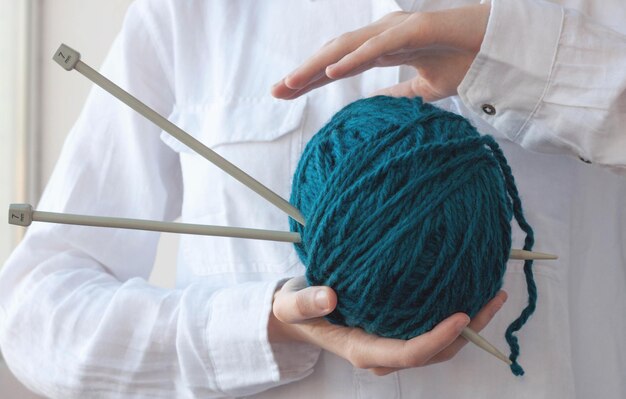 毛糸と編み針の大きなボールが2つの手のひらの間にあります。