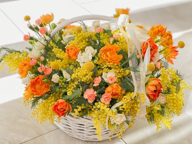 A large beautiful basket with bright yellow flowers. Orange tulips and spring mimosa. A romantic gift for the holiday. Background image of a flower shop