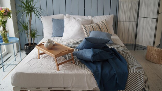 Large bed with pillows and blankets Wooden stand for breakfast on crumpled bed in studio Closeup of interior design room