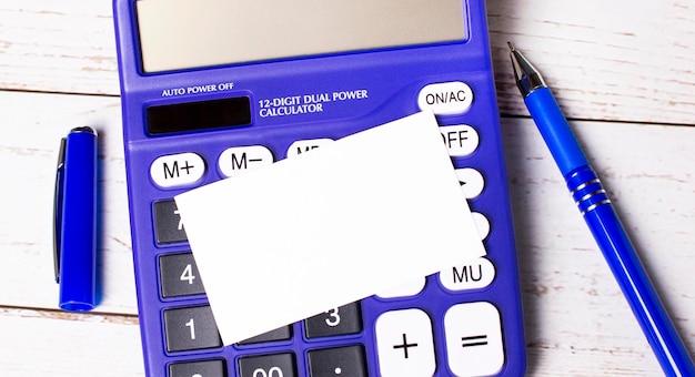 A large blue financial calculator a blue pen and a blank card with a place to insert text on a light wooden background Concept of calculations accounting calculations profit tax with text space