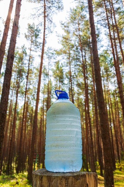 A large bottle of fresh clean drinking water is standing on a stump in the forest drops