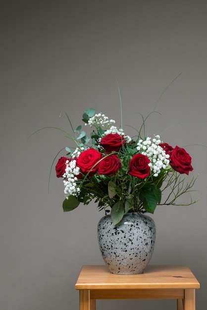 A large bouquet of red roses with white flowers in a gray vase on a gray background Still life