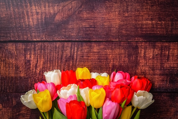 Large bright bouquet of multi-colored tulips on wooden boards of dark brown color.