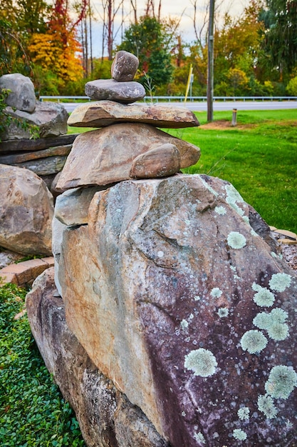 Large cairn stack of rocks with lichen on lawn by road