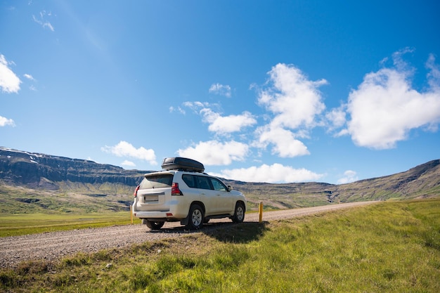 Large car parked on dirt road among the mountain and meadow on sunny day in summer