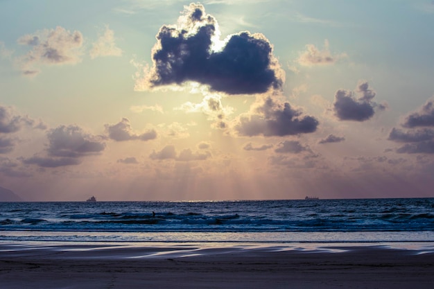 A large cloud is in the sky above the ocean The sun is setting casting a warm glow over the water