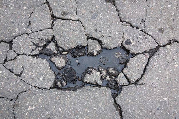 Large cracks on asphalt road filled with water, damage to the road surface in spring