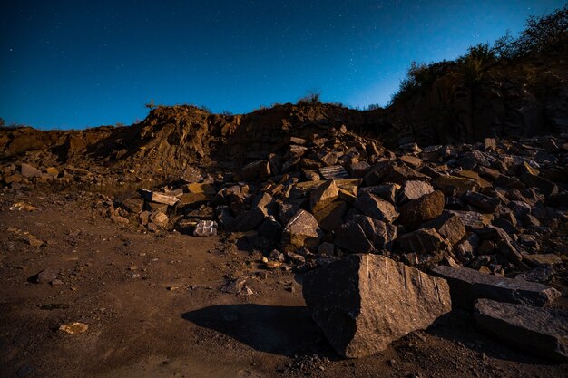 Large deposits of stone materials near a mining mine in the Carpathians against the backdrop of a beautiful night sky with a bright moon