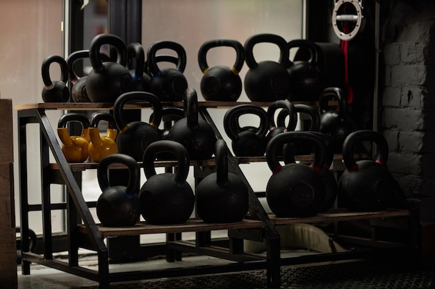 Large display with group of heavy kettlebells of black and yellow color standing on shelves in the corner of modern sports club or gym