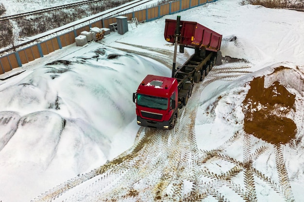 A large dump truck unloads rubble or gravel at a construction\
site in winter car tonar for transportation of heavy bulk cargo\
providing the construction site with materials building in the\
snow