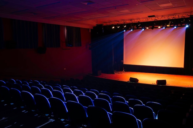 Large empty conference hall with blue empty seats, illuminated lights and a presentation screen