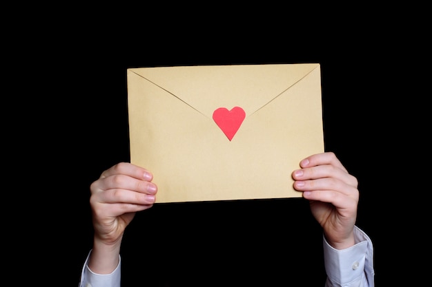 Large envelope with a red heart in children's hands. Close-up.