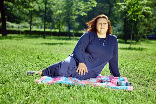 Large european woman with pensive expression sits on mat in middle of lawn