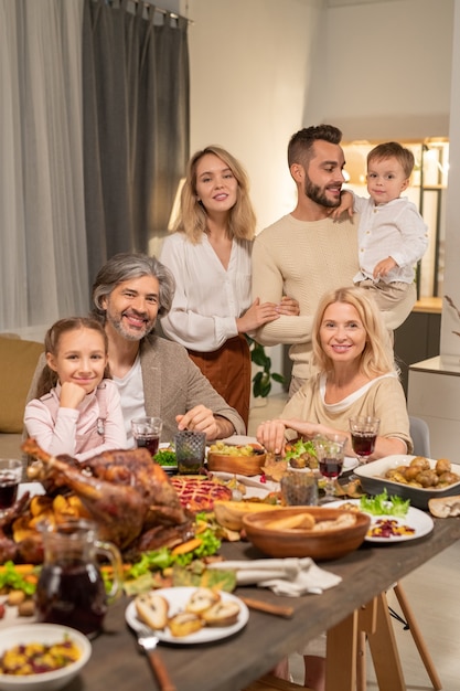 Large family of three generations sitting by festive table served by variety of homemade food and enjoying Thanksgiving dinner together