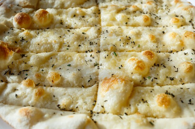 Large freshly baked pizza with spices sprinkled with cheese in bright sunlight.