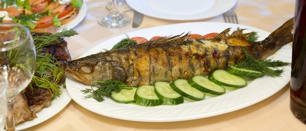 Large fried fish on a platter with vegetables and herbs.,