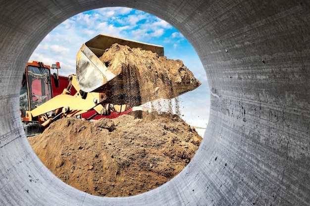 A large front loader pours sand into a pile at a construction site Transportation of bulk materials Construction equipment Bulk cargo transportation Excavation View from a large concrete pipe