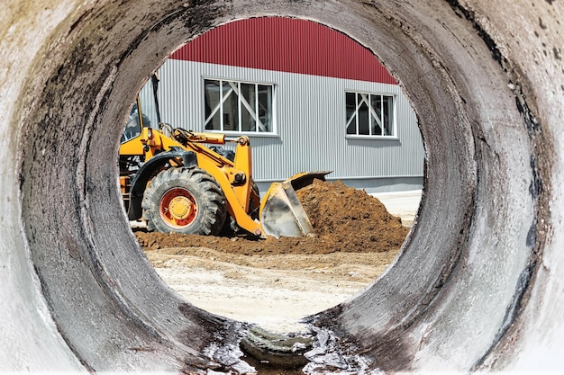 Un grande caricatore frontale versa la sabbia in una pila in un cantiere edile trasporto di materiali sfusi attrezzature per l'edilizia trasporto di merci sfuse scavo vista da un grande tubo di cemento