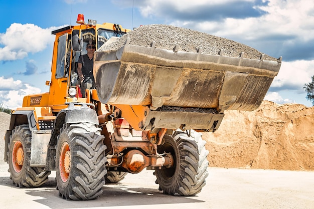 A large front loader transports crushed stone or gravel in a\
bucket at a construction site or concrete plant transportation of\
bulk materials construction equipment bulk cargo\
transportation