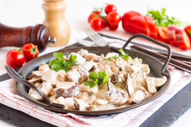 Large frying pan with white mushrooms and cream sauce close-up.