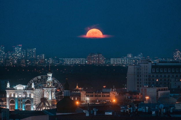 Large full moon over Kyiv in Ukraine with Ferris wheel on Podil and skyscrappers on the background