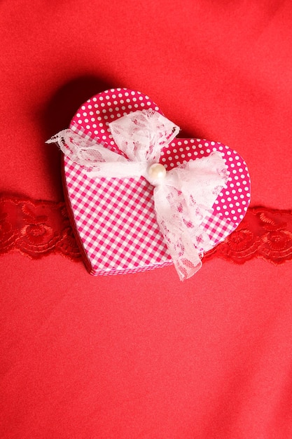 Large gift box in heart shape on red fabric