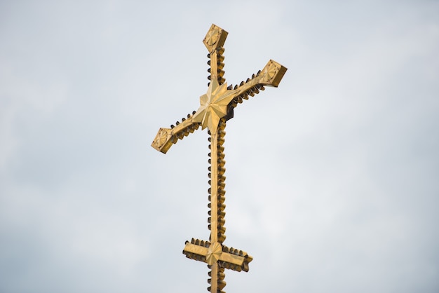 Большой позолоченный церковный крест на фоне серых облаков