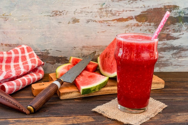 A large glass with a cold watermelon smoothie and some triangles of delicious watermelon