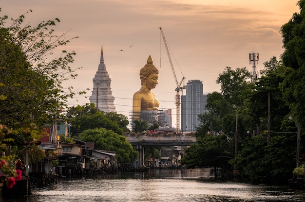 Large golden buddha with pagoda in traditional community on riverside at Bangkok, Thailand