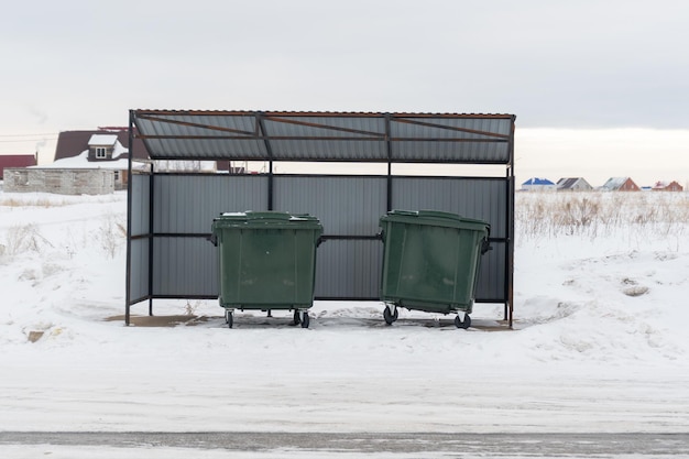 Large green garbage containers in winter under a canopy