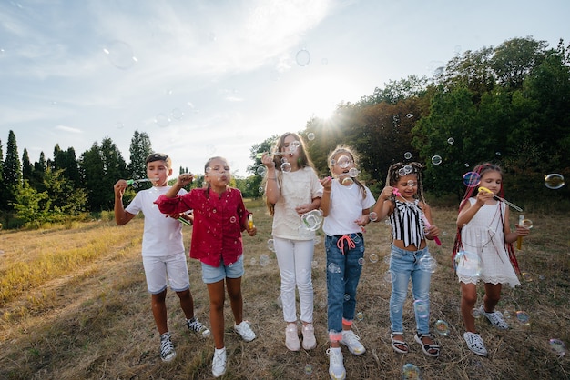 A large group of cheerful children play in the Park and inflate soap bubbles. Games in a children's camp.