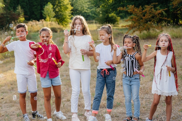 陽気な子供たちの大規模なグループが公園で遊んで、シャボン玉を膨らませます。子供のキャンプでのゲーム。