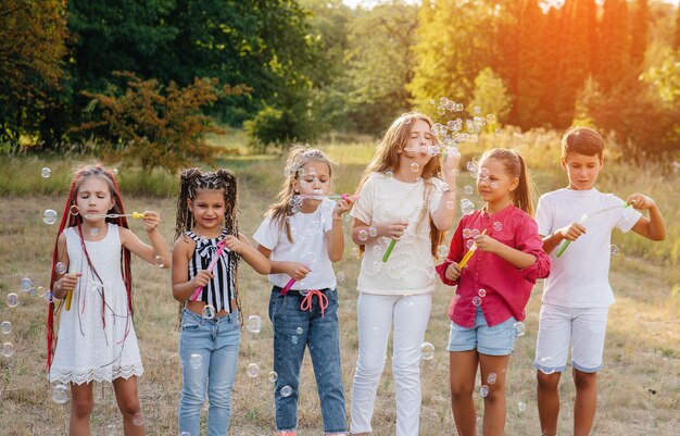 陽気な子供たちの大規模なグループが公園で遊んで、シャボン玉を膨らませます