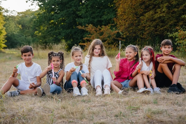 A large group of cheerful children sit on the grass in the Park and smile