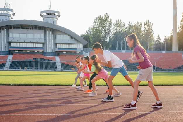 日没時にスタジアムで男の子と女の子の子供たちの大規模なグループが走り、スポーツをします健康的なライフスタイル