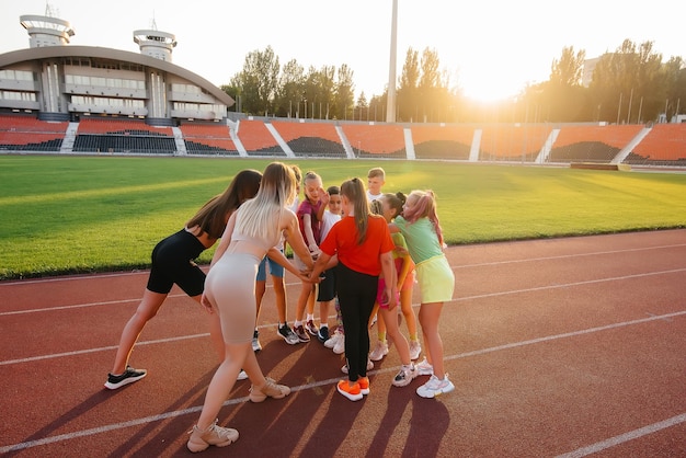 Foto un folto gruppo di bambini, ragazzi e ragazze, stanno insieme in cerchio e incrociano le mani sintonizzando e sollevando lo spirito di squadra prima della partita allo stadio durante il tramonto uno stile di vita sano