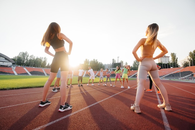 Un folto gruppo di bambini, ragazzi e ragazze, si riscalda e si allena sotto la guida di un allenatore allo stadio durante il tramonto uno stile di vita sano