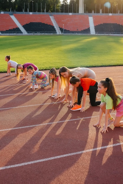 A large group of  girls, are taught by a coach at the start before running at the stadium during sunset. A healthy lifestyle.