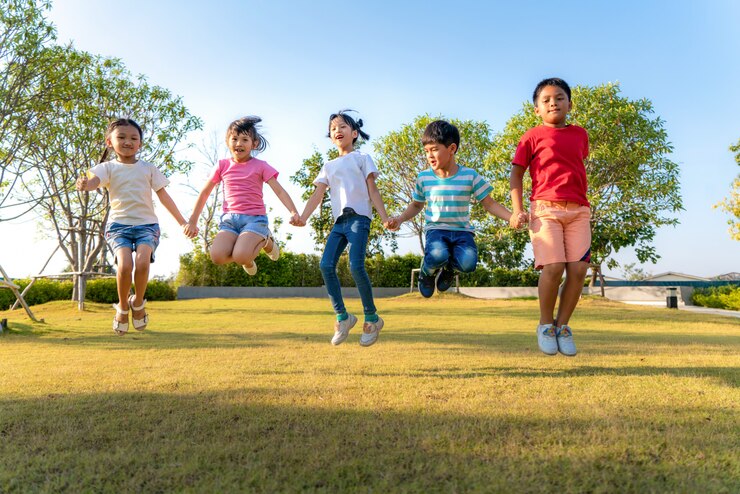 都市公園でのカジュアルな服で晴れた日の間に遊んで、一緒にジャンプ手を繋いでいる幸せなアジア笑顔幼稚園の子供の友人の大規模なグループ。