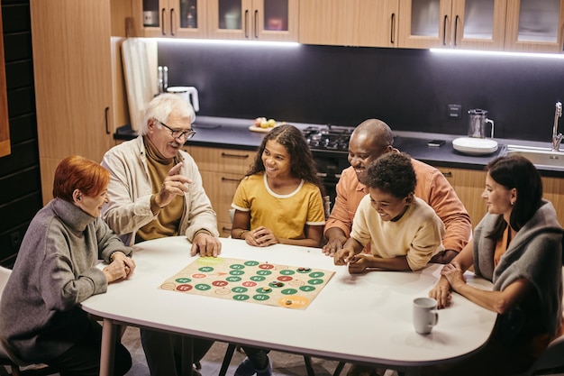 Photo large happy multiracial family playing board game by table