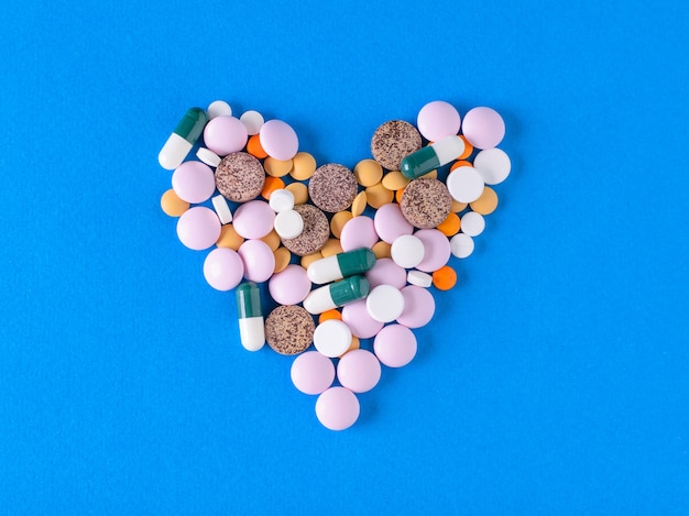 A large heart of colorful pills on blue background.