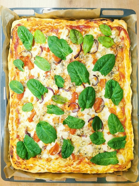 Large homemade pizza on a square baking sheet with spinach tomatoes cheese ketchup onions garlic