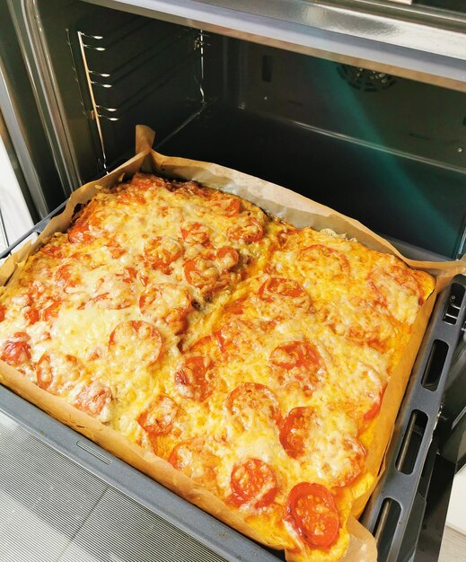 Large homemade pizza on a square baking sheet with tomatoes and other products Homemade fast food