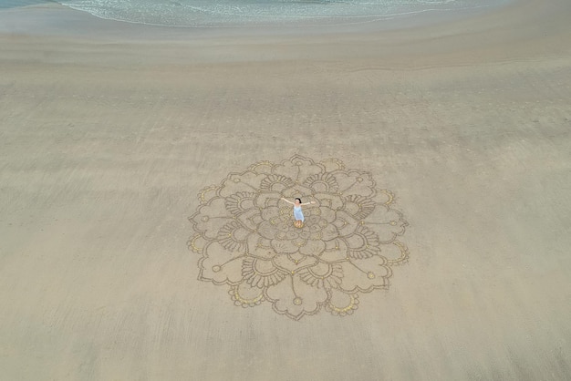 Большая мандала, нарисованная на песке у океана с девушкой посередине