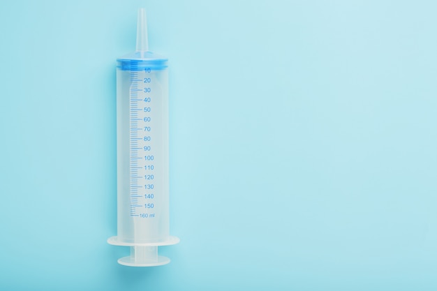 A large medical syringe on a blue background with a scale, a copy of the space. The concept of minimalism.