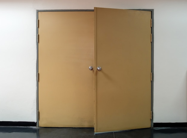 The large metal door was left ajar after someone entered the filing room in the office, empty the people around the metal door, front view for the copy space.