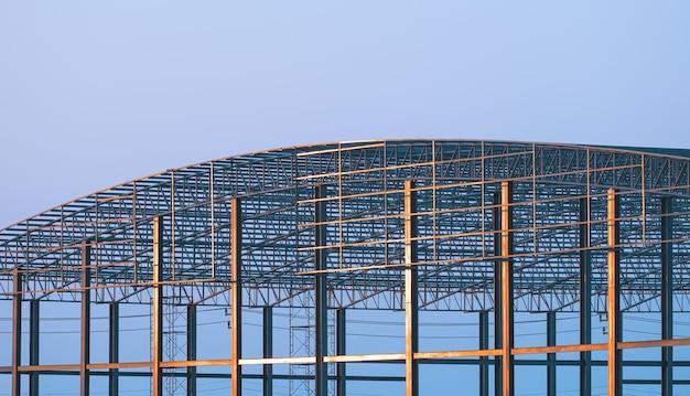 Large metal factory building with dome roof structure in construction site against evening sky