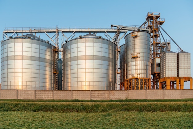 A large modern plant located near a wheat field for the storage and processing of grain crops view of the granary illuminated by the light of the setting sun against the blue sky harvest season