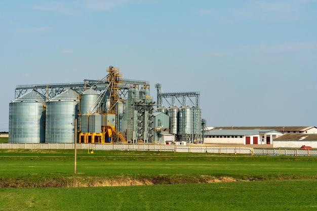 A large modern plant for the storage and processing of grain crops view of the granary on a sunny day against the blue sky End of harvest season silver silos on agro manufacturing plant